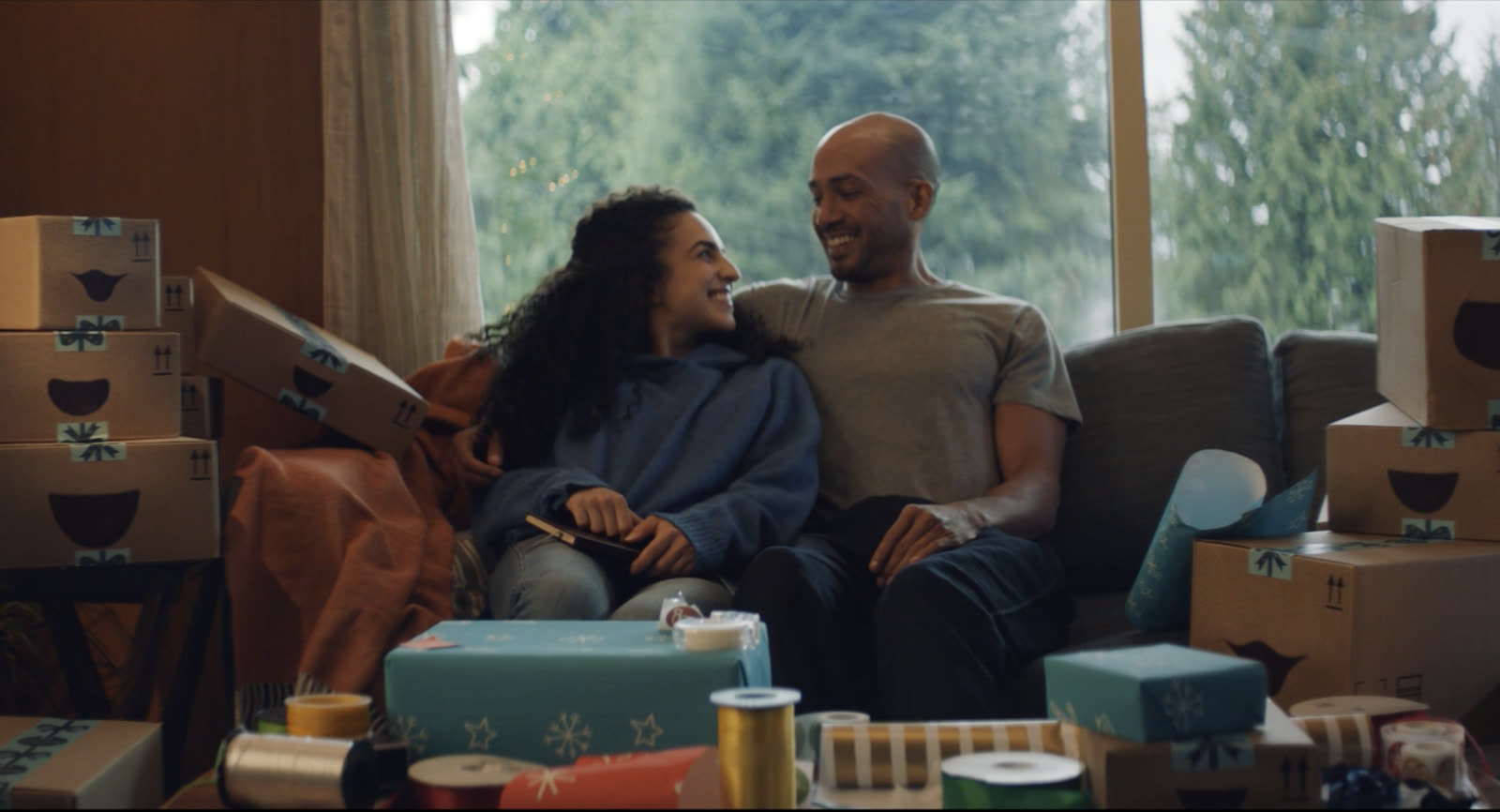 A couple laughing on a sofa surrounded by delivery boxes