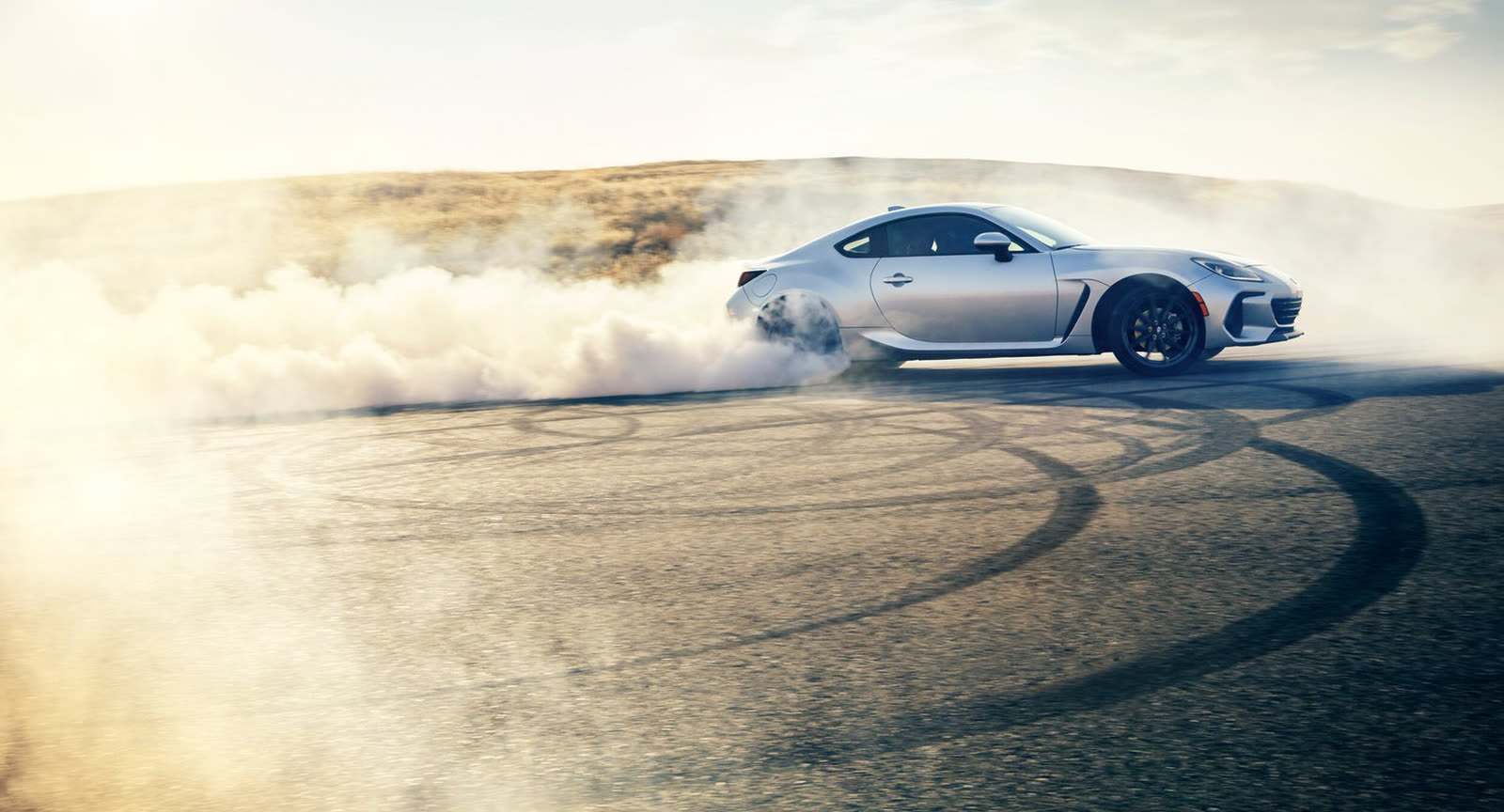 A silver sports car drifting through dust on a dry lake bed